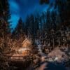 Fotografia di una baita in mezzo al bosco con il cielo "nell'ora blu" e alcune luci accede sul patio della casa