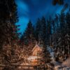 Fotografia di una baita in mezzo al bosco con il cielo "nell'ora blu" e alcune luci accede sul patio della casa